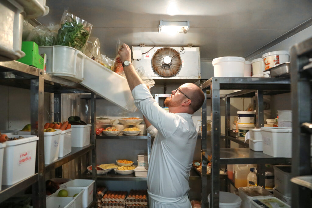 A chef grabbing ingredients from his working walking in refrigerator.